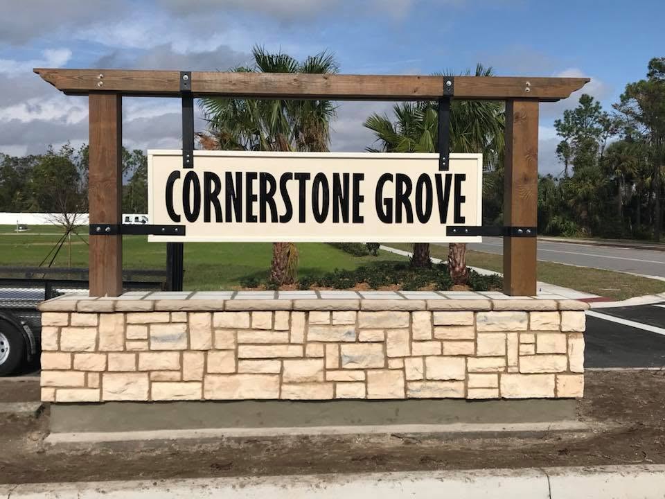 Cornerstone Grove entrance sign with black letters on a cream panel hung from a wood frame over a stone base in Port Orange, FL