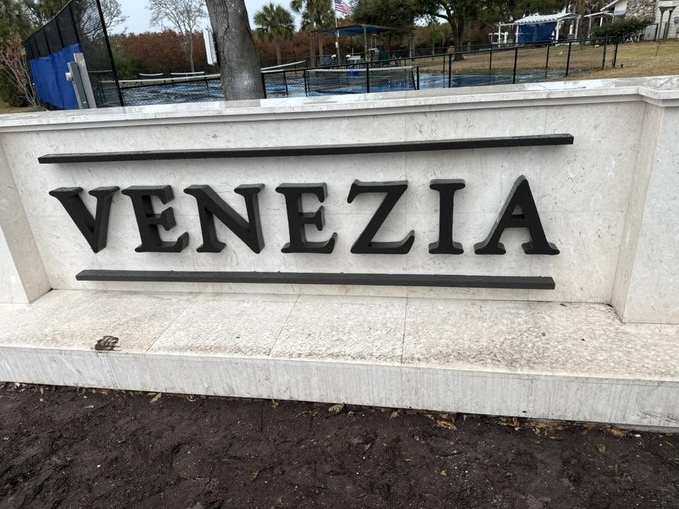 Venezia community monument sign with dimensional dark metal letters on a coral stone wall in New Smyrna Beach, FL