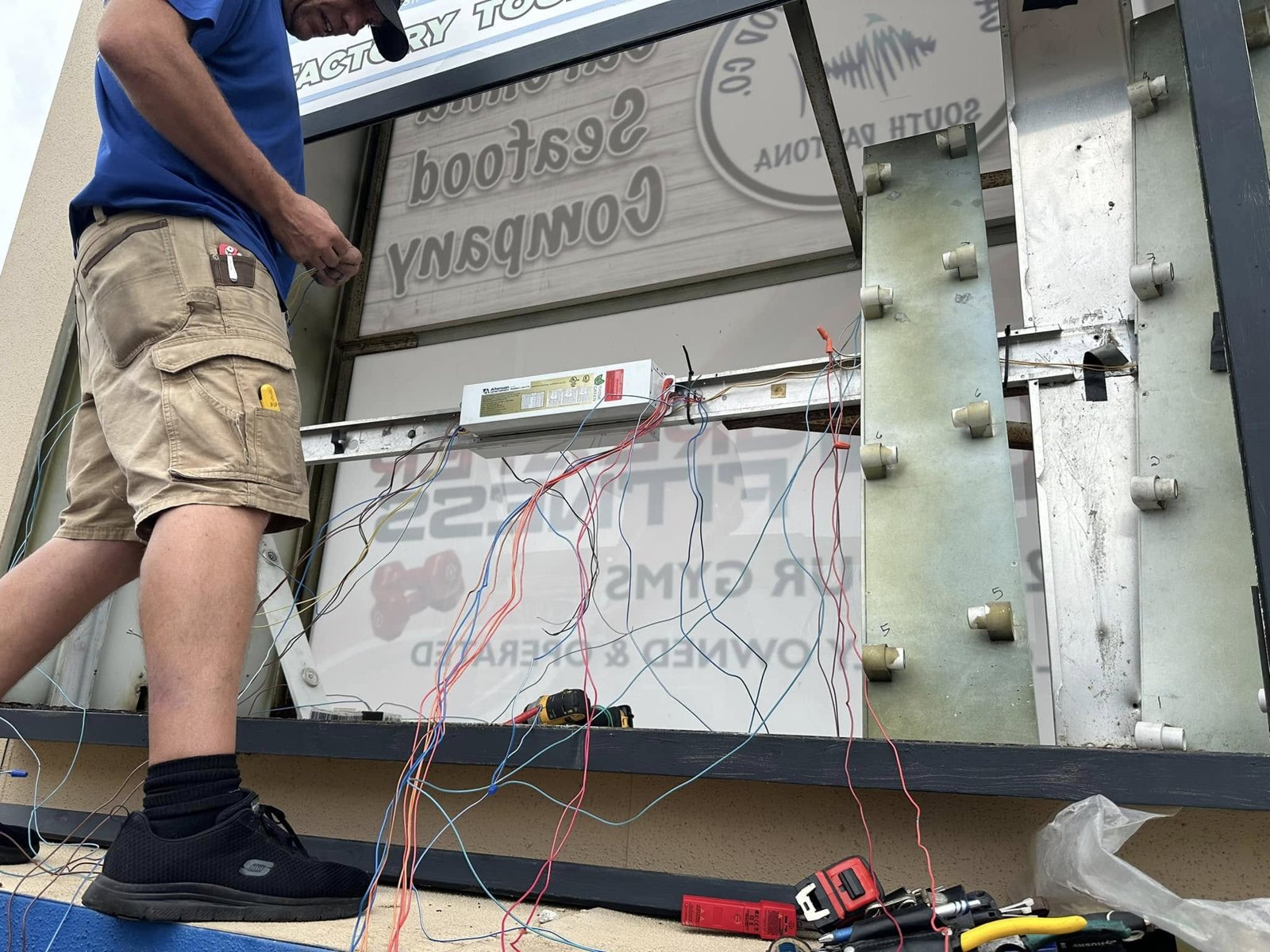 SOS Sign & Lighting technician rewiring the lamps and ballast inside an opened illuminated sign cabinet