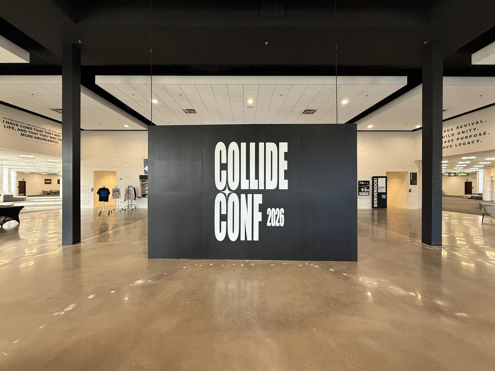 Large white vinyl Collide Conf 2026 lettering on a black wall in a conference lobby